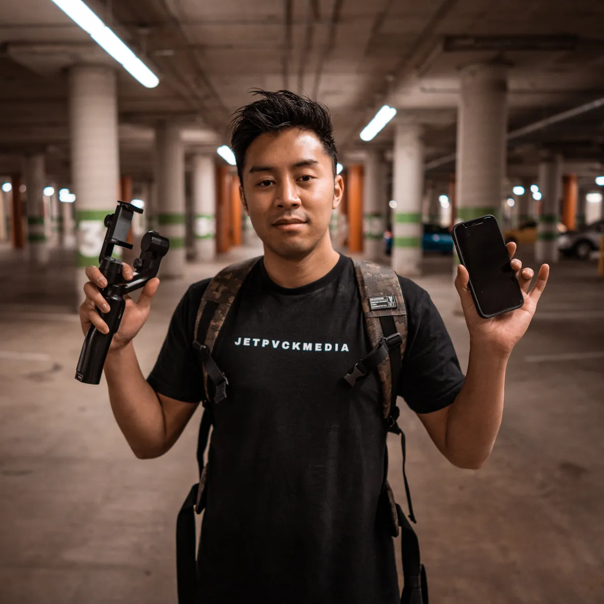 Jet Kamchamnan, founder of JETPVCK MEDIA, holding a gimbal and phone in a JETPVCK MEDIA t-shirt in Atlanta